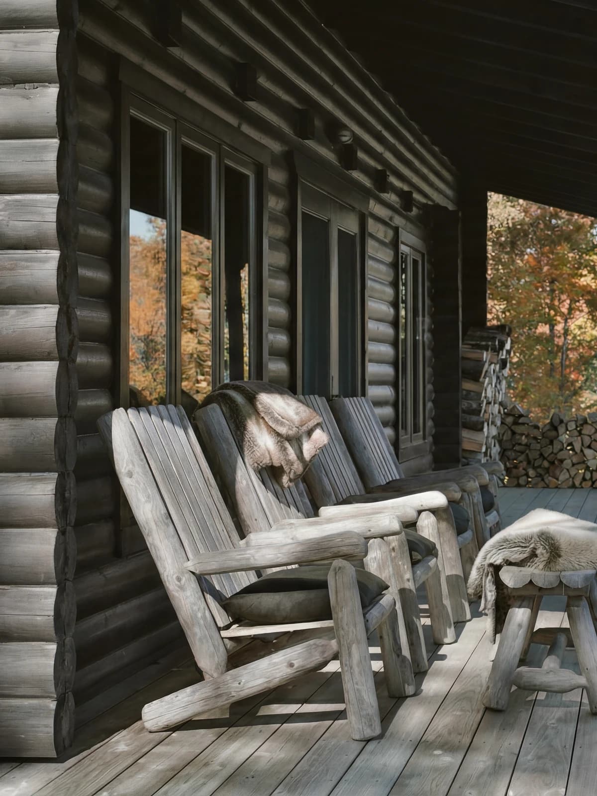 Wooden rocking chairs and fur throws on the cabin porch, autumn forest beyond