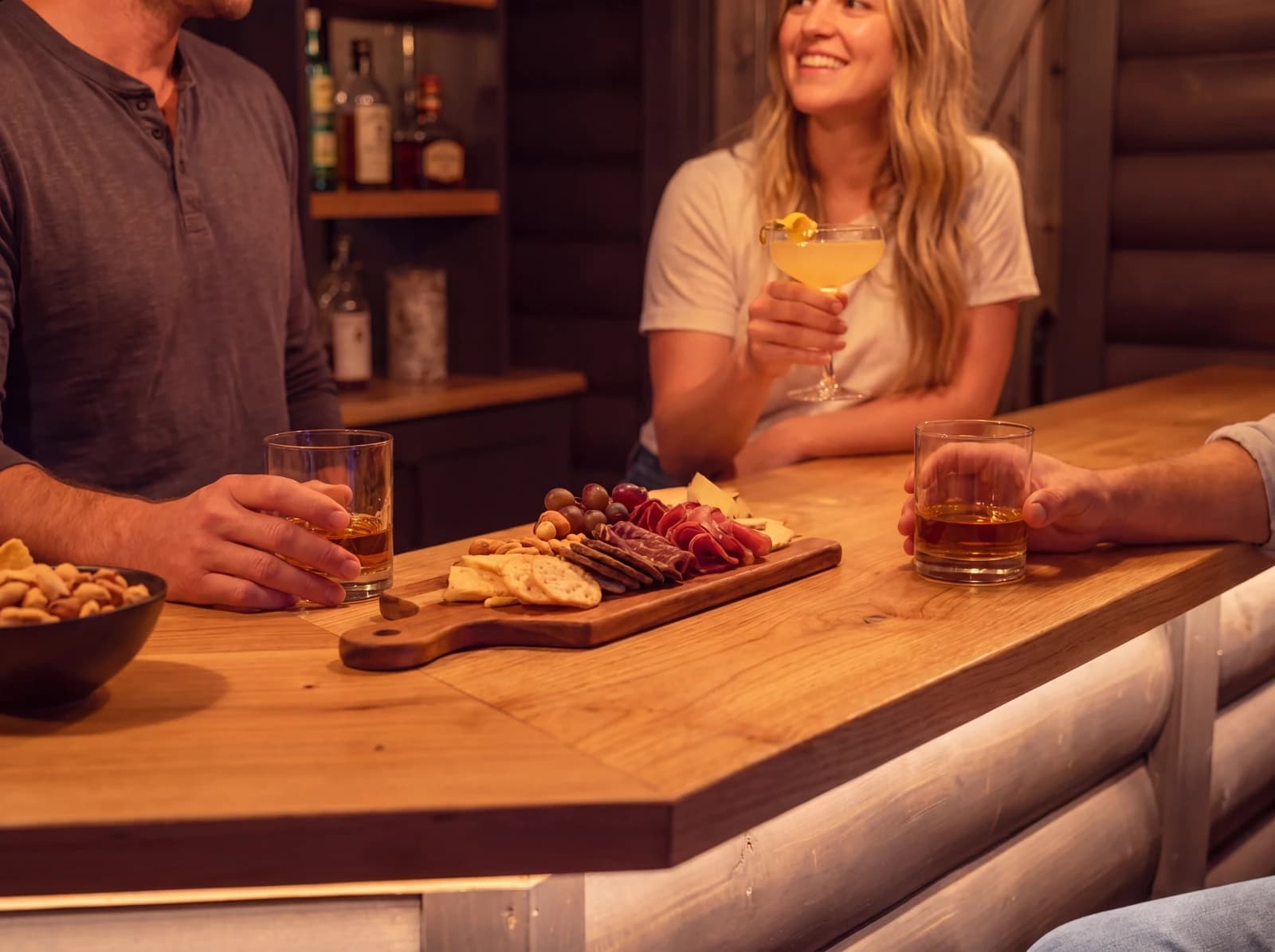 Three friends laughing at the bar with a charcuterie board and cocktails