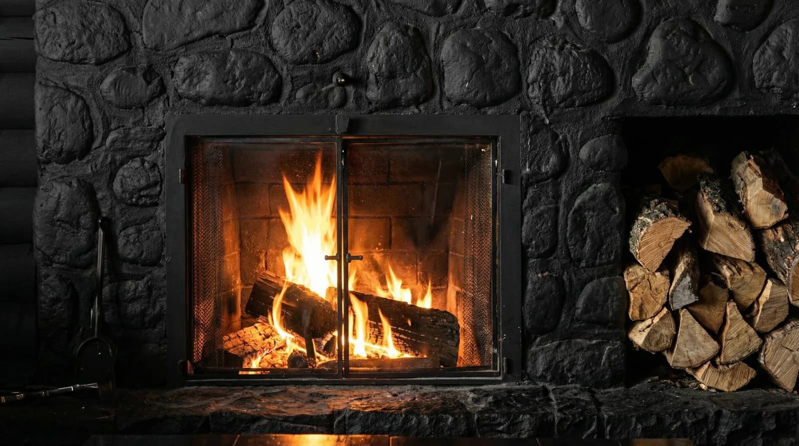 Stone fireplace with a wood fire and stacked logs